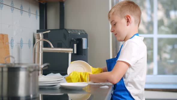 Side View of Cute Boy Washing Dishes in Modern Home Kitchen