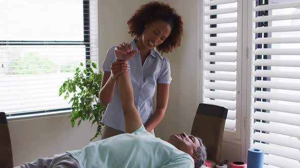 Mixed race female physiotherapist helping senior man stretching his arm