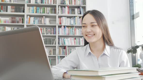 Charming Asian Woman Laughing While Using Laptop at the Library