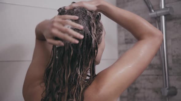 Back Look of Woman Washes Head with Shampoo Under Shower