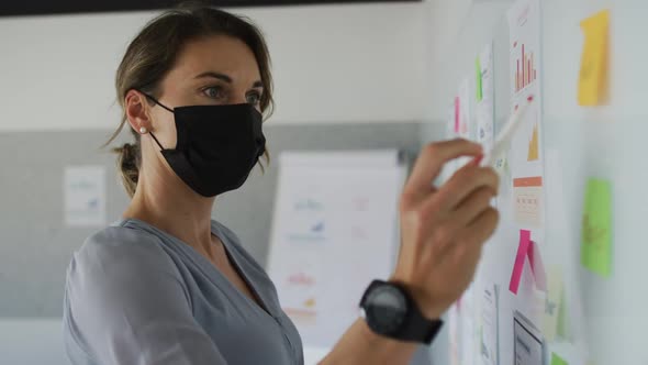 Caucasian businesswoman wearing face mask, making notes