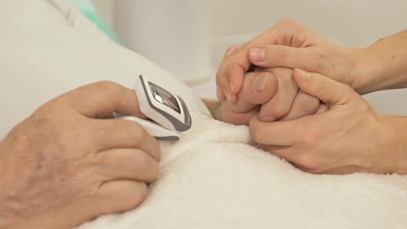 Female Hand Holds the Hand of an Elderly Patient with Severe Symptoms Lying on a Bed in an Emergency