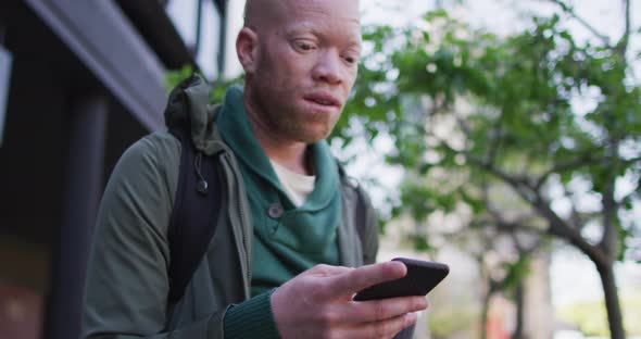 Thoughtful albino african american man with dreadlocks drinking coffee and using smartphone