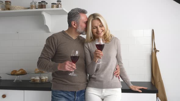 Happy Middleaged Wife and Husband Holding Glasses of Wine and Hugging at Home