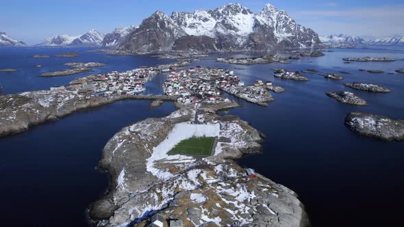 Forwarding aerial shot of Henningsvaer with scenic mountains in the background and worlds famous soc