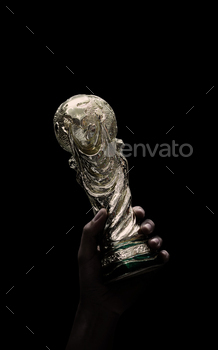 A World Cup Trophy in hand and Black Background. Man holding a trophy of the FIFA World Cup in hand. Fifa 2022 winning trophy is raised up in the air.