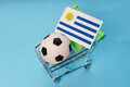 Soccer ball with Uruguayan flag in shopping cart on blue background. Football cup earnings. - PhotoDune Item for Sale