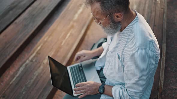 Elderly Man Types Text for Project Sitting on Stairs in City