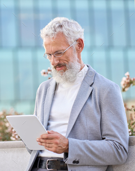 Old senior professional business man using digital tablet standing outdoors.
