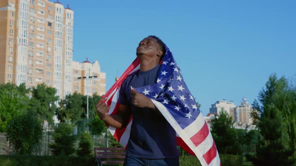 Happy African Man Walks in Park with USA Flag on Shoulders