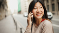 Attractive Asian woman looking cheerful talking over smartphone enjoying day out. City life concept - PhotoDune Item for Sale