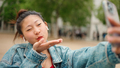 Asian girl wearing wireless earphones sending kiss taking selfie for her social media outdoors - PhotoDune Item for Sale