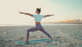 Attractive yogi girl in sportswear looking good standing in warrior yoga pose on beach - PhotoDune Item for Sale