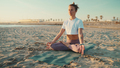 Beautiful blond woman dressed in sportswear sitting in lotus pose by the sea - PhotoDune Item for Sale