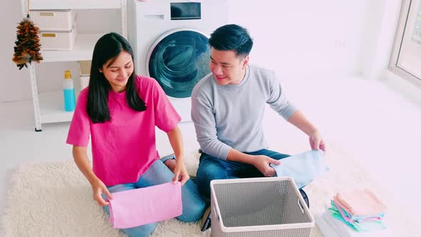 Husband helping his wife folding clothes. Happy Asian couple spending time together at home.