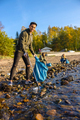 Smiling young man cleaning the ocean with volunteers on sunny day - PhotoDune Item for Sale
