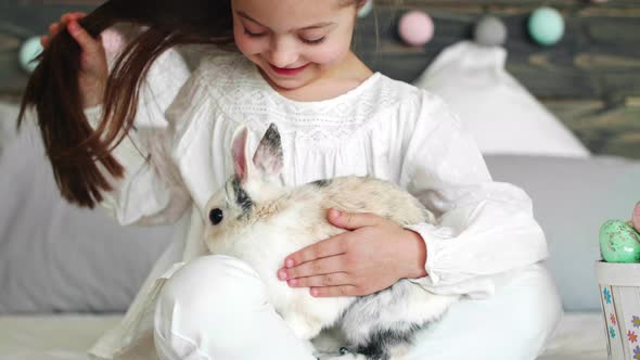 Girl sitting next to easter basket and stroking the rabbit