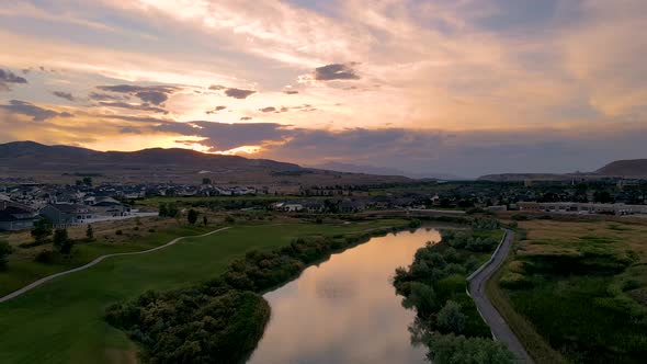 Flying above a river and golf course at sunset with the colorful sky reflecting off the surface of t