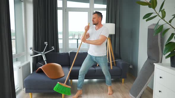 Man Fooling Around While Cleaning the House and Singing Into a Mop Instead of a Microphone