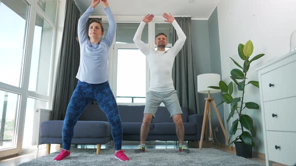 Caucasian Couple is Doing Jumping Jacks Exercise at Home in Cozy Bright Room Slow Motion