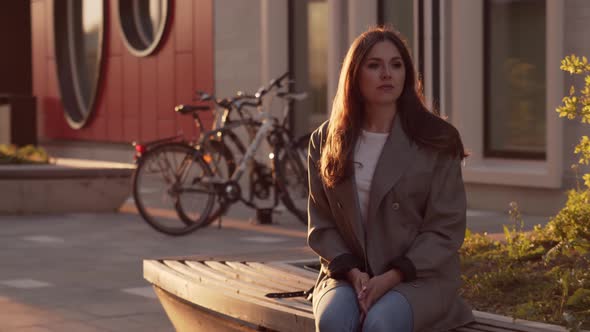 Young attractive business woman sitting outdoor on the bench. Sunset light.