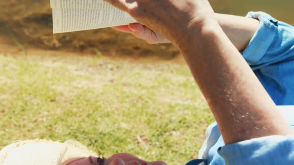 Senior woman reading a book while lying on the bench in the park