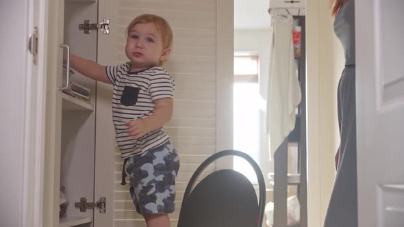 A Little Baby Crawls Onto a Chair Next to an Open Closet and His Mom Takes Out Colorful Pencils for