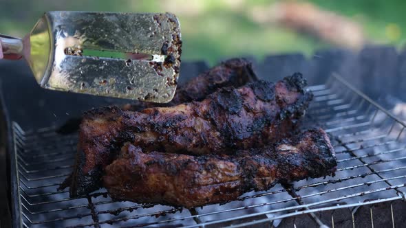 Flipping Delicious Beef or Pork Ribs Frying on a Charcoal Grill with Tongs