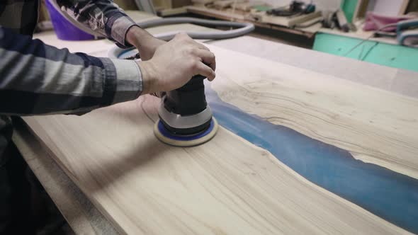 The Carpenter Processes the Surface of a Wooden Tabletop with a Grinder