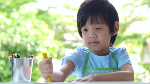 Cute Asian Child Drawing With Crayons On White Table