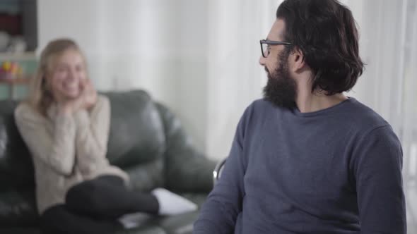 Young Caucasian Man Looking Back at His Happy Pregnant Wife, Turning To Camera and Expressing