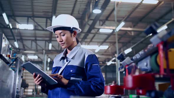 Engineer is using a tablet to check the machine's control system in a factory.