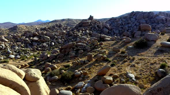 Fly over some big boulders in the desert of southern California with clear sky and no clouds.