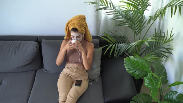 Young woman drinking tea and using mobile smartphone while having skin care spa day at home