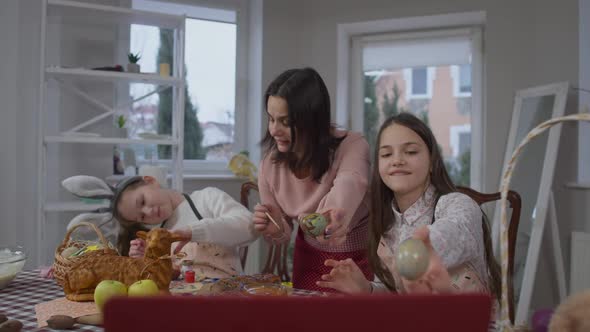 Cheerful Mother and Daughters Bragging Colored Eggs on Easter Online Using Video Chat on Laptop