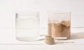 Whey protein powder with chocolate flavor in a spoon next to a glass of water. wellness product  - PhotoDune Item for Sale