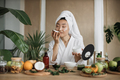 Young asian woman in white bathrobe and towel holding half of coconut and making homemade cream - PhotoDune Item for Sale