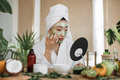Attractive asian woman looking at mirror sitting at table with ingredients for homemade cosmetics - PhotoDune Item for Sale