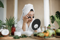Asian woman sitting at table in white towel and bathrobe, looking at mirror and applying patches - PhotoDune Item for Sale