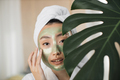 Young healthy asian woman with green cosmetic mask hiding her face behind monstera leaves. - PhotoDune Item for Sale