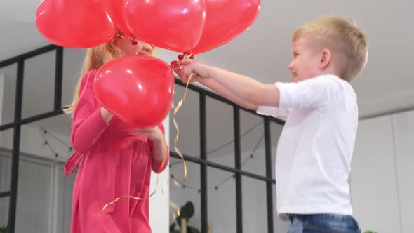 Little Boy and Girl Dancing with Red Heart Shape Balloons at Home