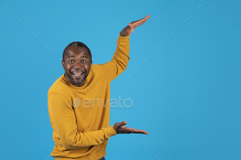 l outwear holding something invisible transparent in his hands and smiling over blue studio background, copy space
