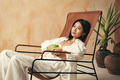 Asian woman lying on lounger on spa resort, holding cup of coffee in hands - PhotoDune Item for Sale