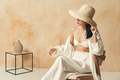 Elegant asian woman in beach hat, covering her eyes, sitting on chair on brown textured wall - PhotoDune Item for Sale