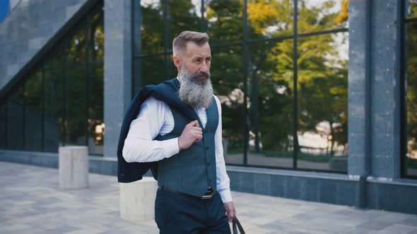 Handsome Bearded Mature Man in Suit Walking Outdoors on Modern Building Background During Sunny Day