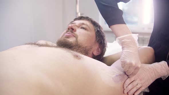 A Man Lies on a Couch and Talking with the Master While She Tears the Wax Off His Armpit