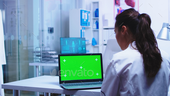 n private clinic wearing white coat while nurse in blue uniform checking patient results on computer.