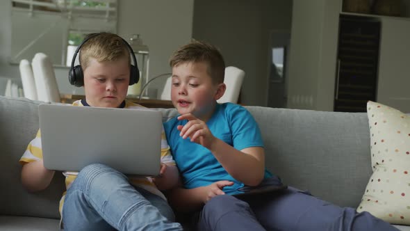 Caucasian boy with his brother sitting in living room and using laptop