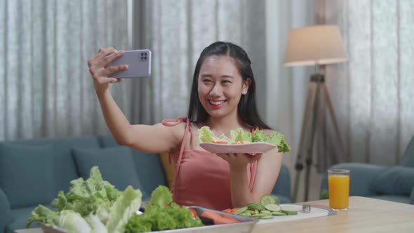 Asian Woman Holding A Dish Of Healthy Food And Taking Selfie With Smartphone While Sitting At Home