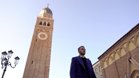 Young Man in Deep Blue Coat Walks Along Ancient City Street